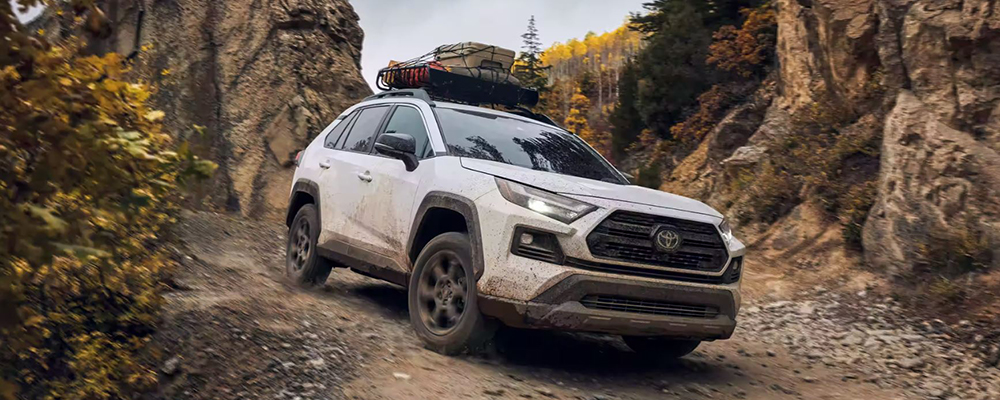 A white Toyota RAV4 drives off-road in the mountains.