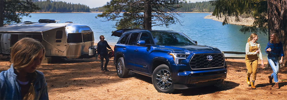 A blue Toyota Sequoia parked along the shore of a beach, hauling a camper.
