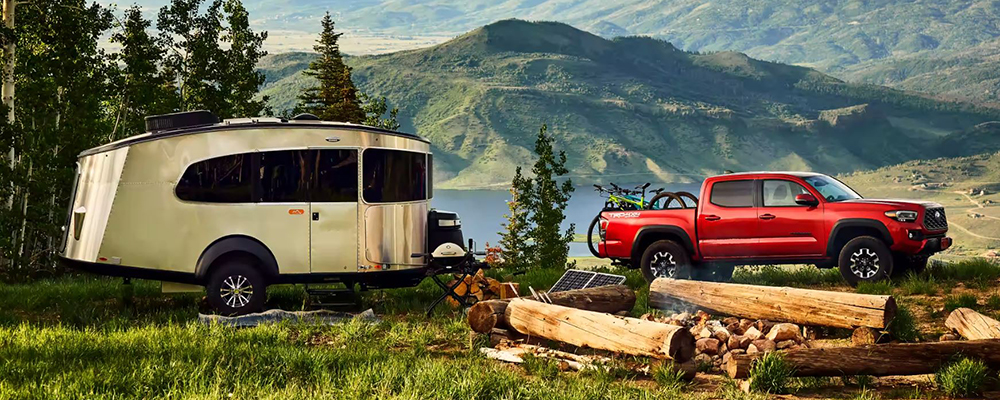 A red Toyota Tacoma is parked at a campsite on the edge of a lake.